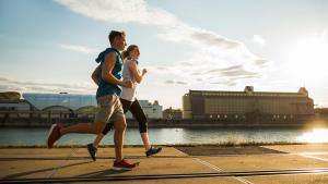 Ragazzo e ragazza che corrono sulla banchina vicino alla riva di un fiume al tramonto per migliorare la salute fisica e mentale, benefici della corsa, riduzione infiammazione, salute cardiovascolare.