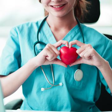 Dottoressa in camice bianco e stetoscopio tiene un modello di cuore stilizzato per illustrare i benefici cardiovascolari della corsa, come miglioramento dell'apparato cardio-circolatorio e riduzione del rischio di malattie cardiache