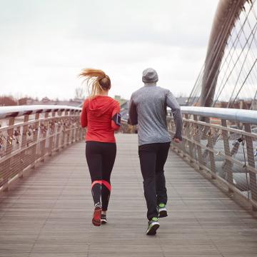 Ragazzo e ragazza che corrono di spalle su un ponte verso l'orizzonte, simboleggiando il viaggio verso una vita più lunga, sana e felice attraverso i benefici della corsa